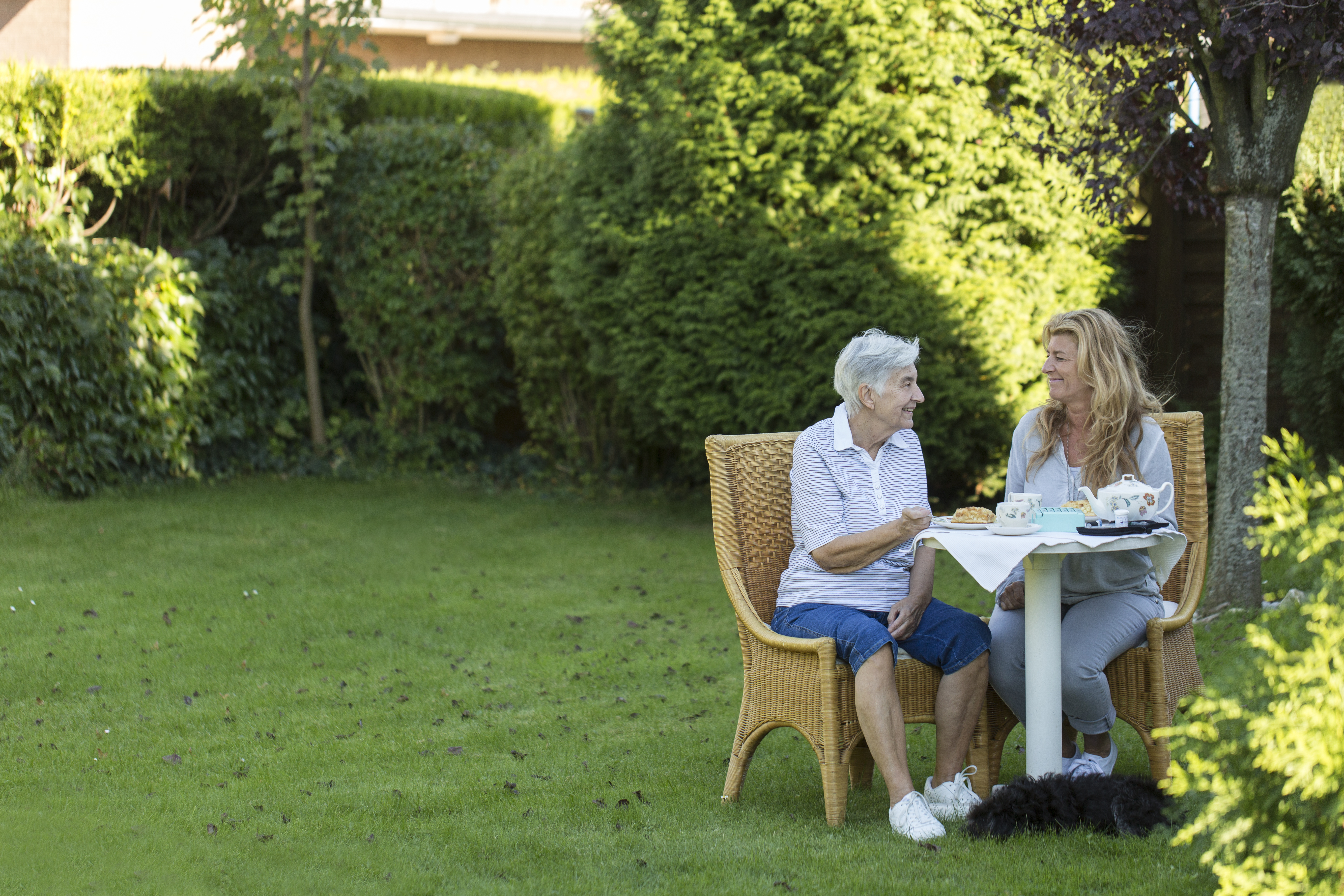 Zwei Frauen, eine alt und eine jung, sitzen im Garten und trinken Kaffee.